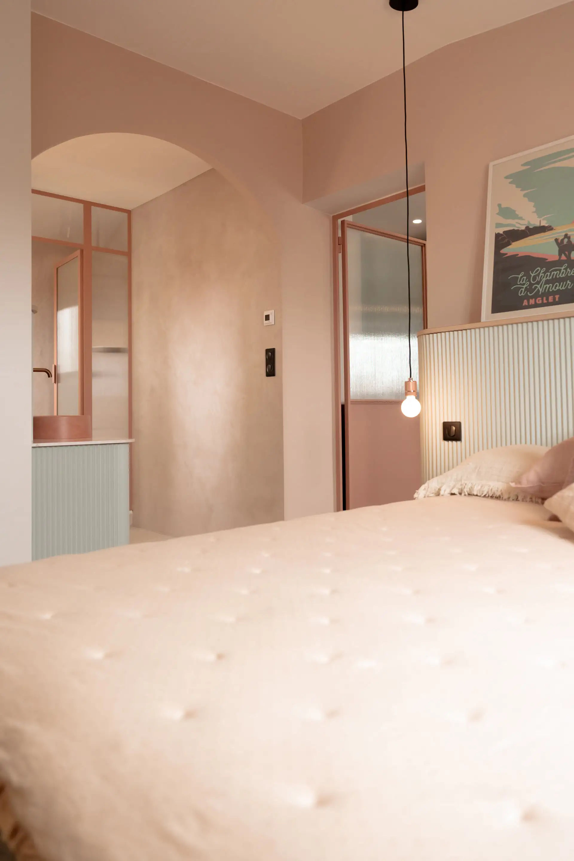 Lit aux coussins rose poudré devant une arche en miroir