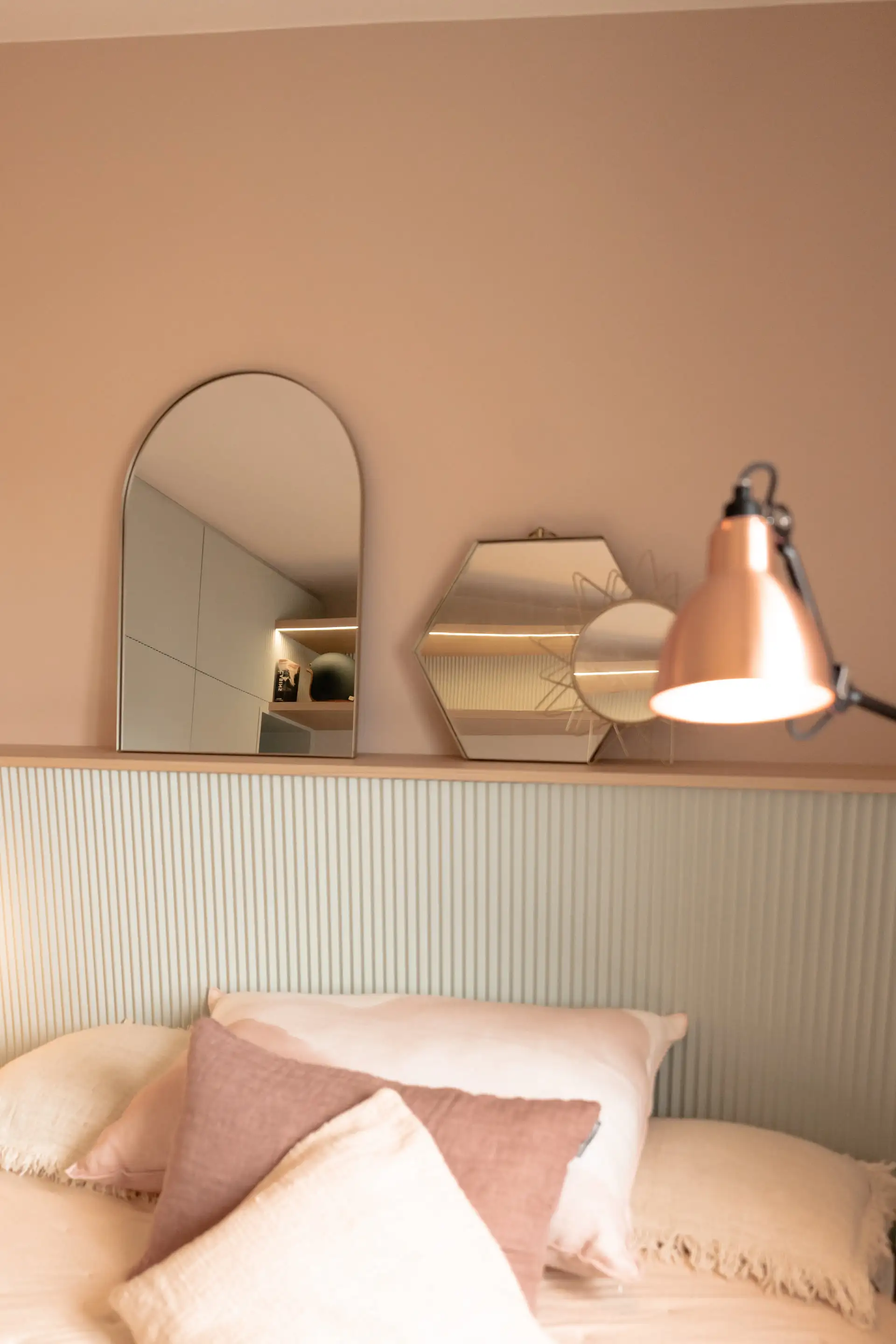 Lampe cuivrée et miroir hexagonal au-dessus du lit