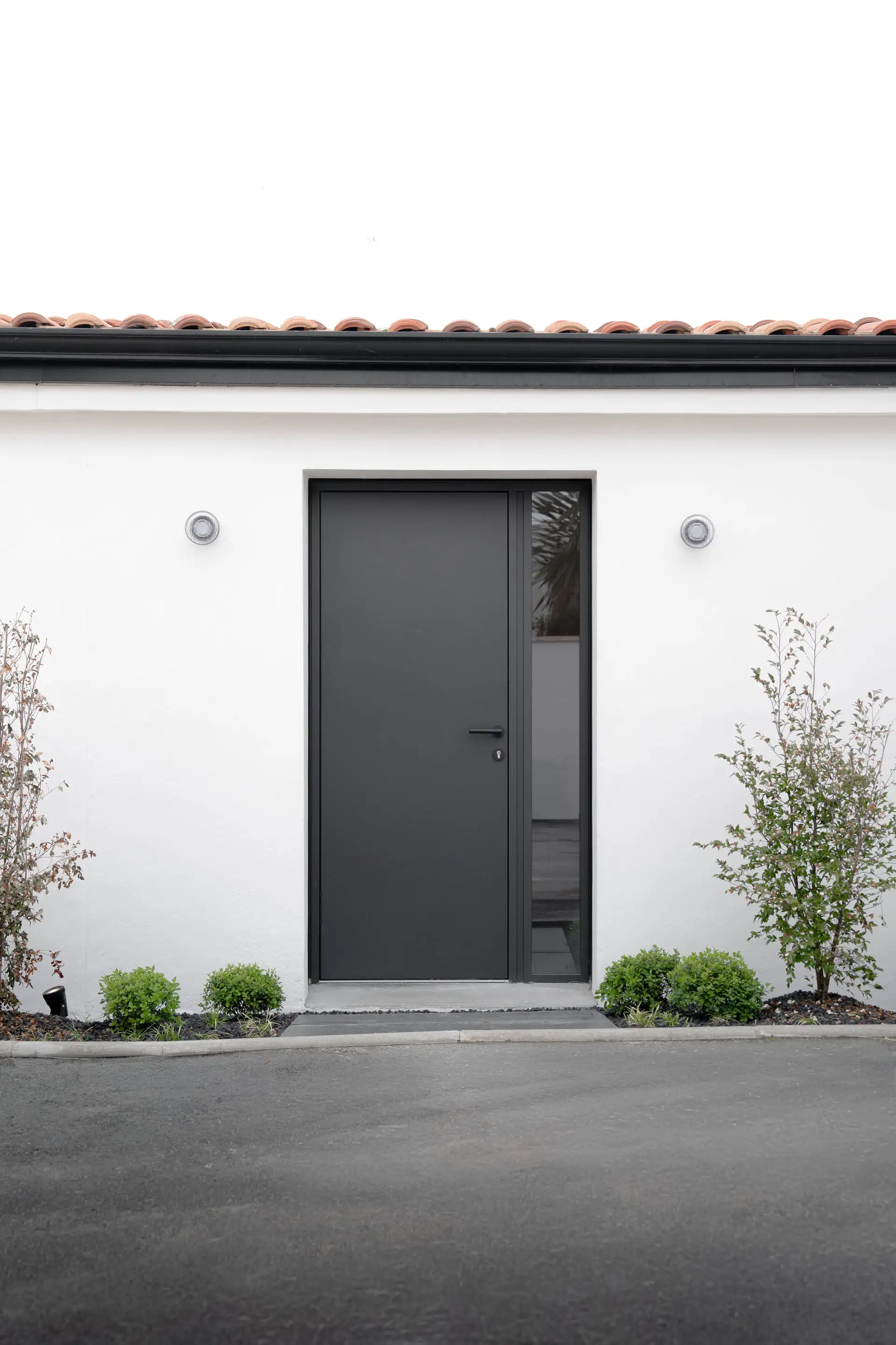 Porte d’entrée anthracite dans la façade blanche, plantations au pied