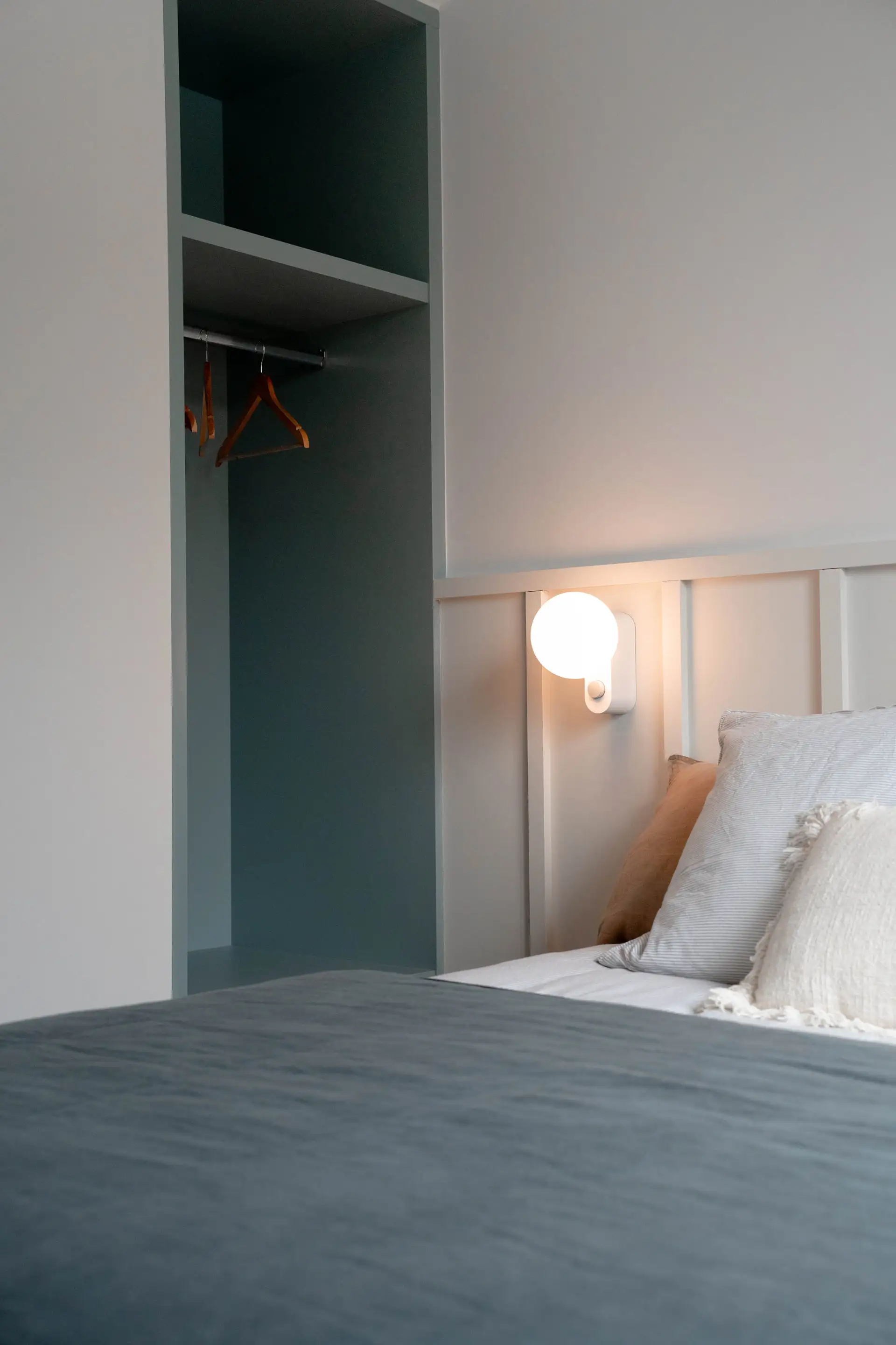 Lit et penderie ouverte dans une chambre aux tons gris-bleu