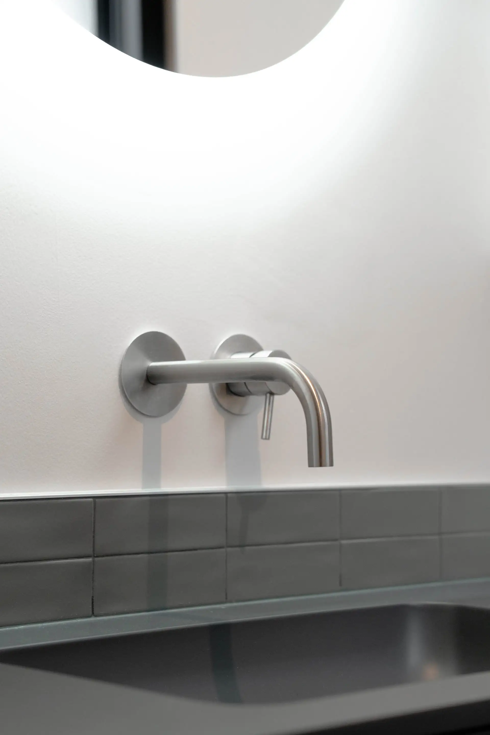 Robinetterie murale en inox au-dessus d’une vasque gris foncé