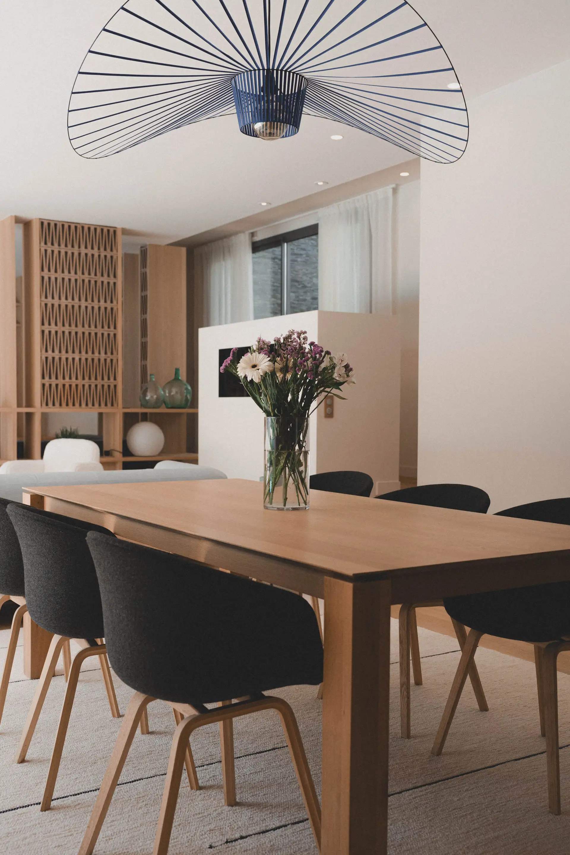 Table en chêne, chaises noires et suspension bleue au-dessus d’un bouquet