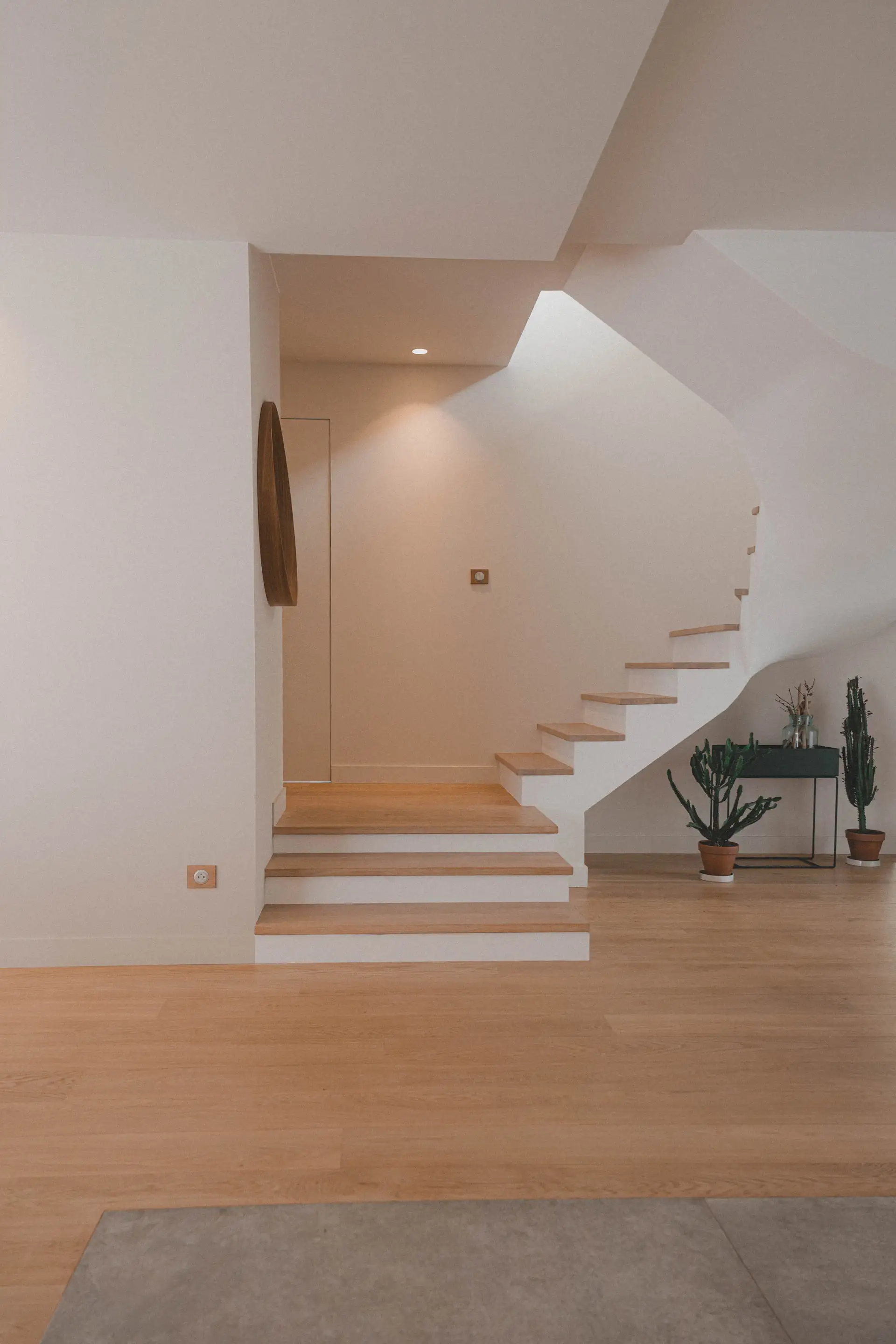 Escalier blanc à marches de chêne et miroir rond dans l’entrée