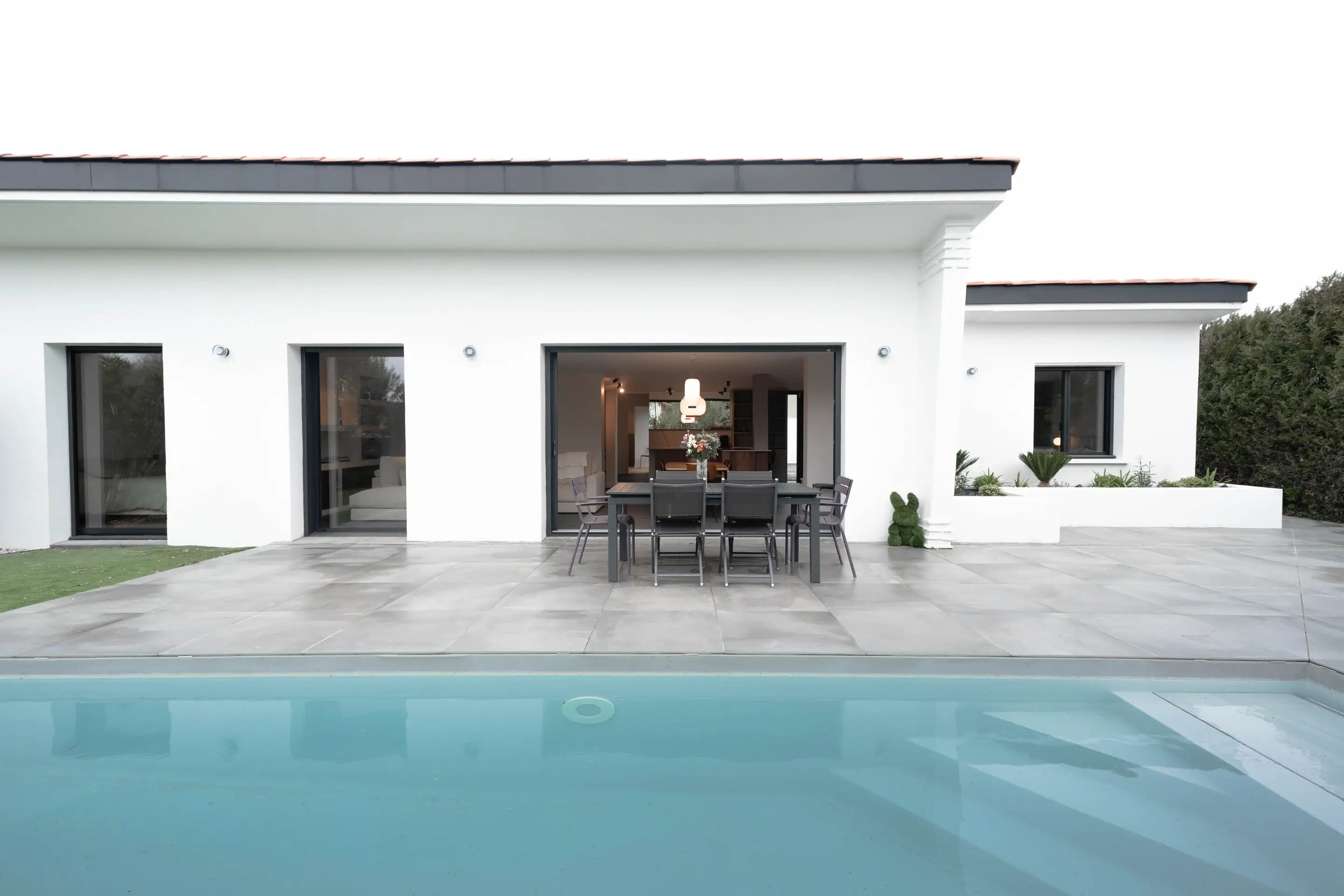 Façade blanche de plain-pied et terrasse en dalles ouvrant sur la piscine
