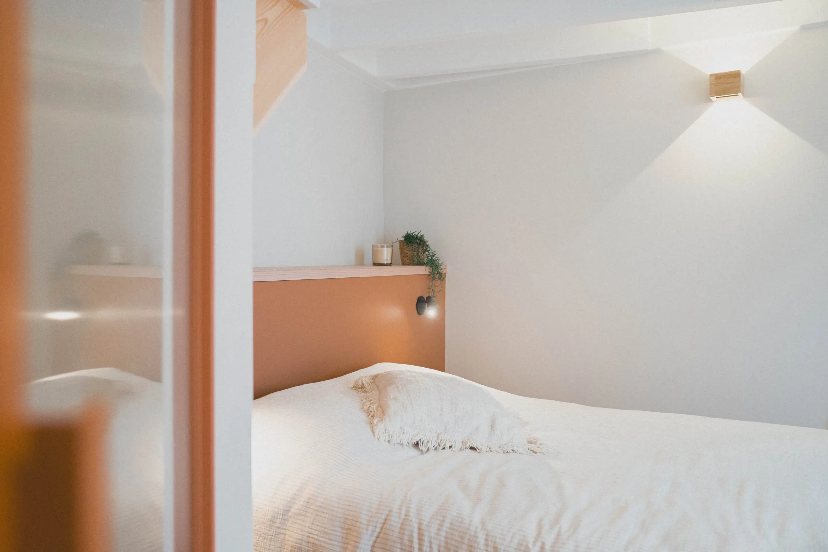 Lit aux draps blancs vu depuis la porte vitrée encadrée de bois orangé