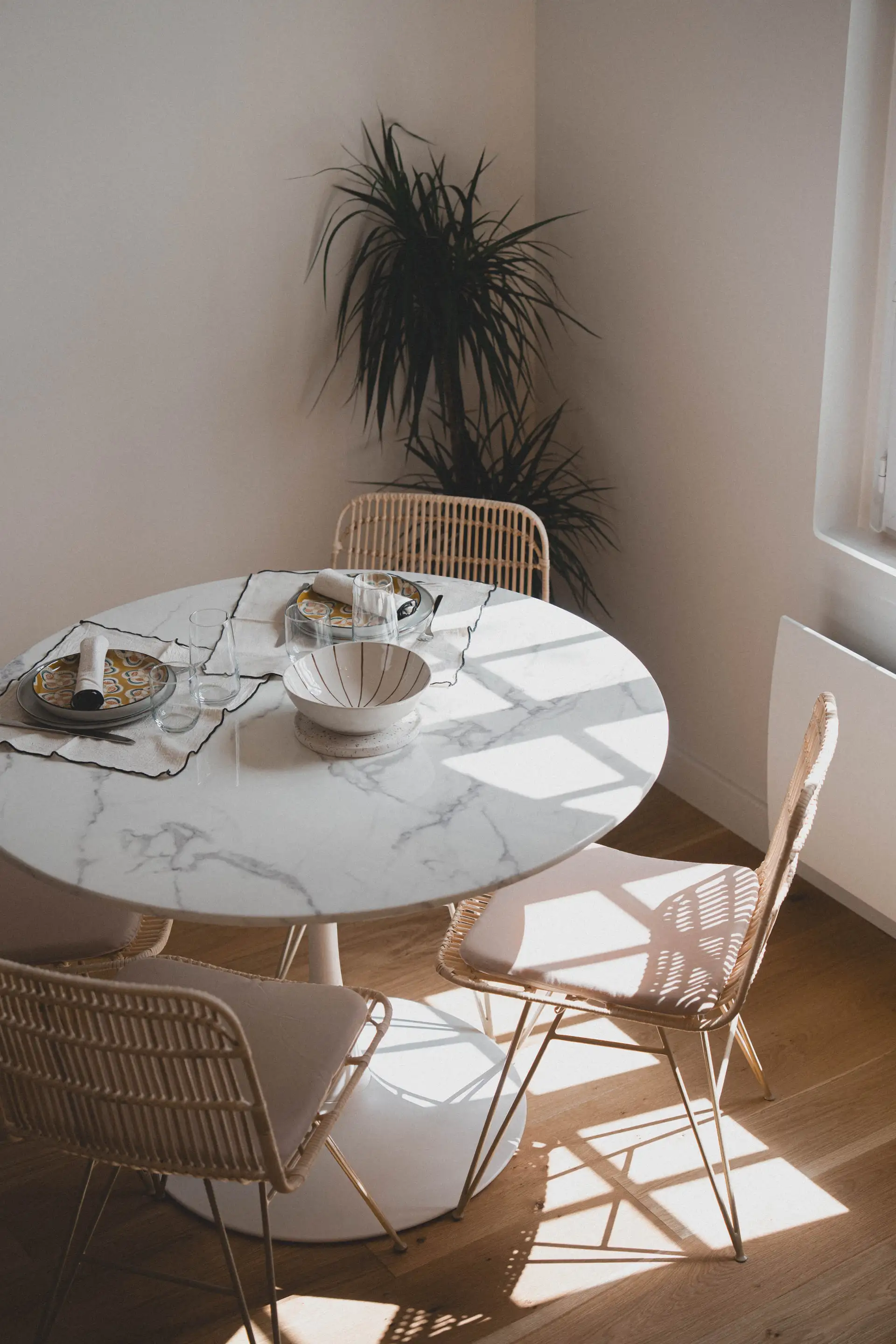 Table ronde dressée et chaises en rotin dans la lumière du matin