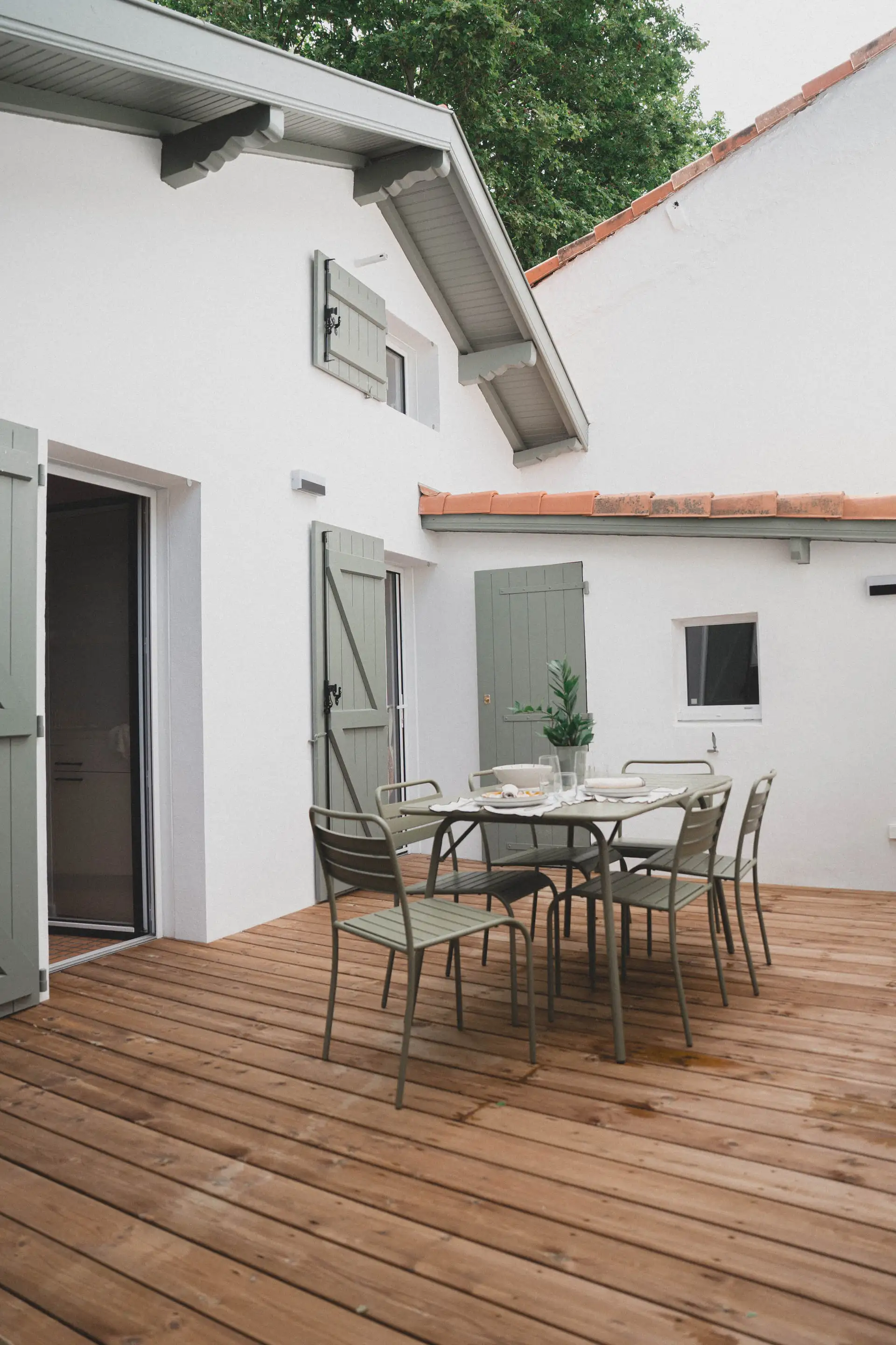 Terrasse en bois à l’arrière de la maison, table et chaises vert sauge